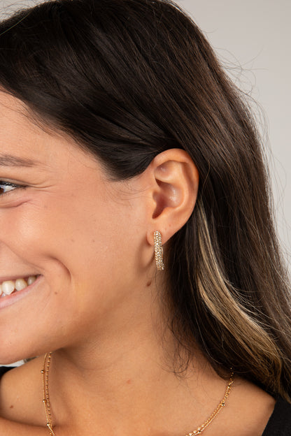 Close-up of a woman wearing gold hoop earrings with a neutral background