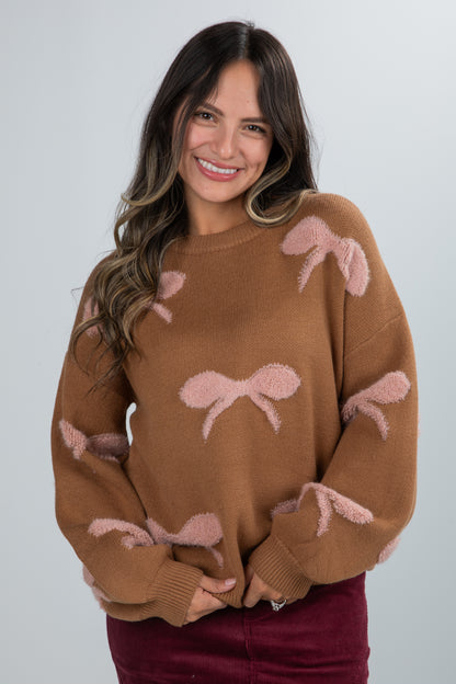 Woman wearing a brown sweater with pink bow designs on a plain background
