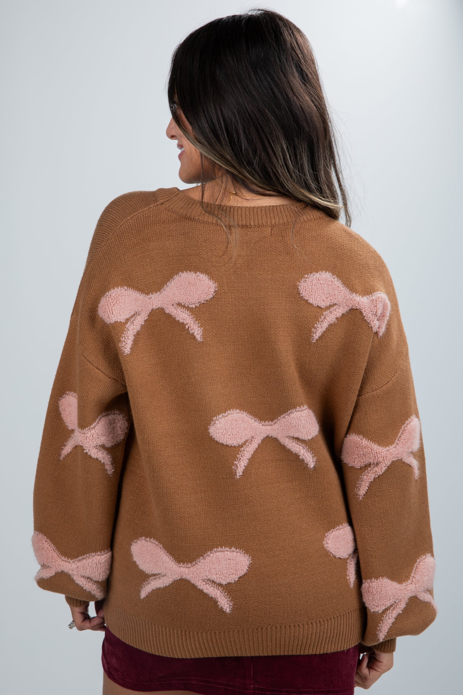 Brown sweater with pink bow patterns worn by a person against a white background