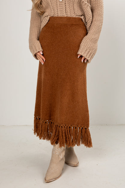 Person wearing a brown fringed skirt and beige sweater on a white background