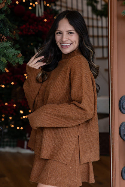 Woman in a brown outfit standing in front of a decorated Christmas tree.