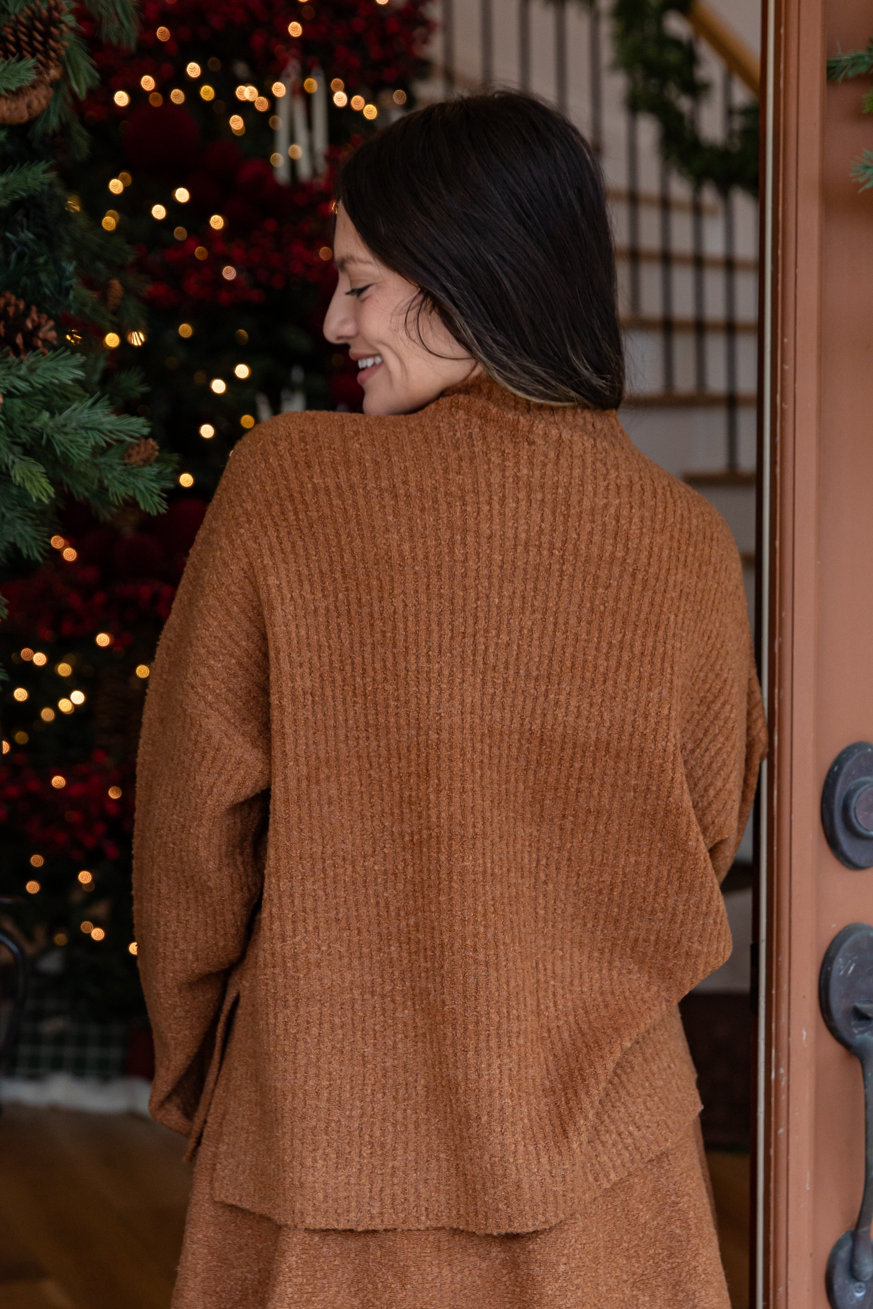 Woman wearing a brown coat standing in front of a decorated Christmas tree.