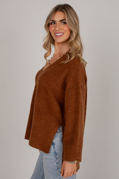 A woman wearing a brown fuzzy knit sweater and light blue jeans, photographed against a plain light gray studio background.