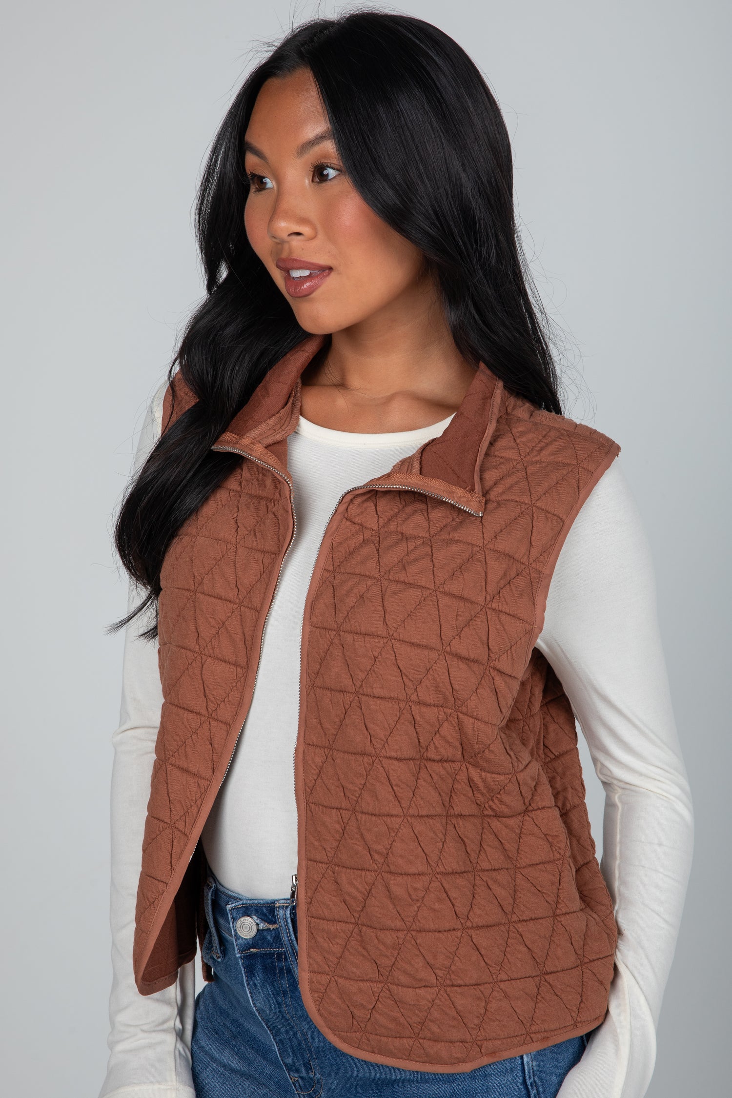 Woman wearing a brown quilted vest over a white shirt on a gray background