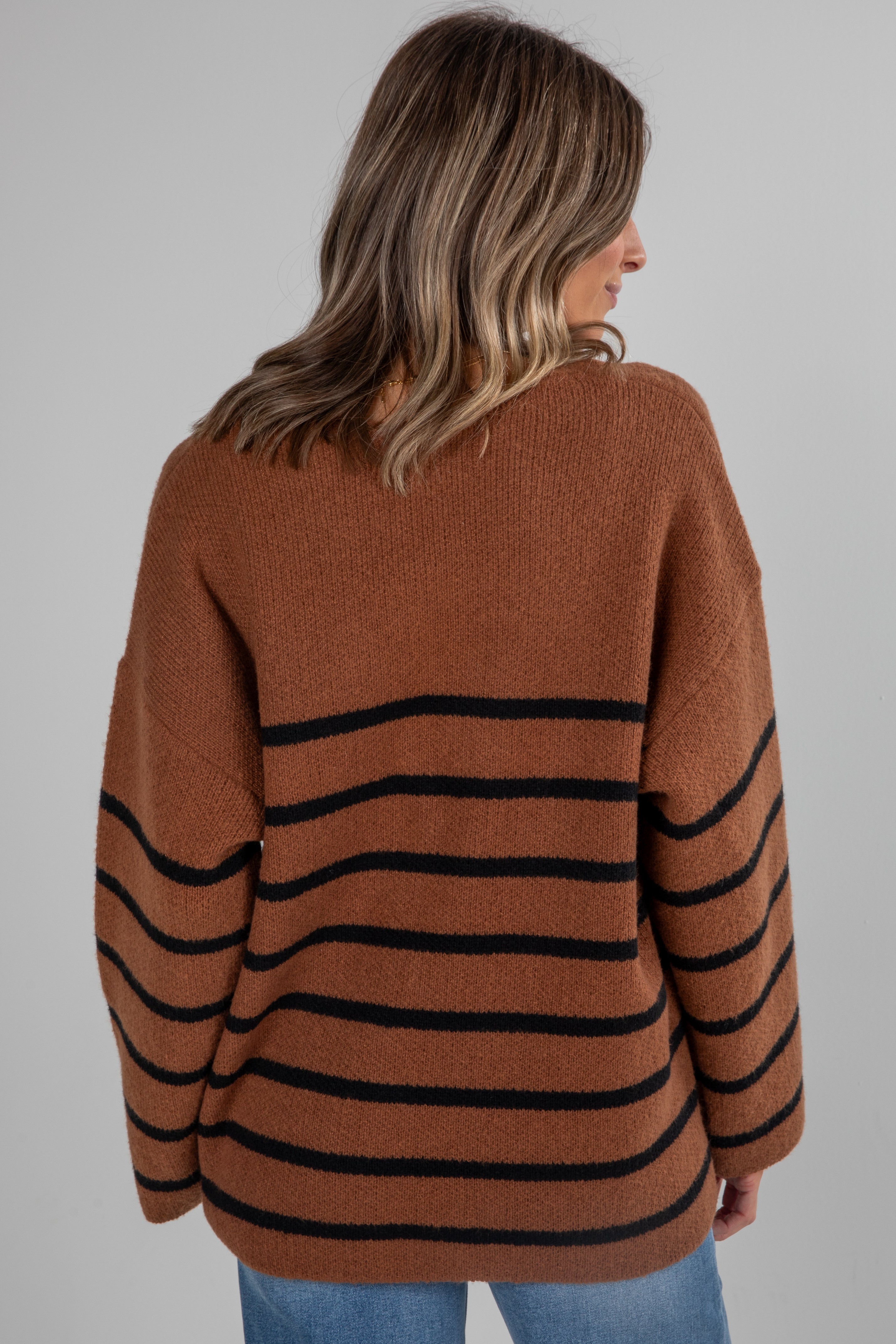 Woman wearing a brown sweater with black stripes on a gray background