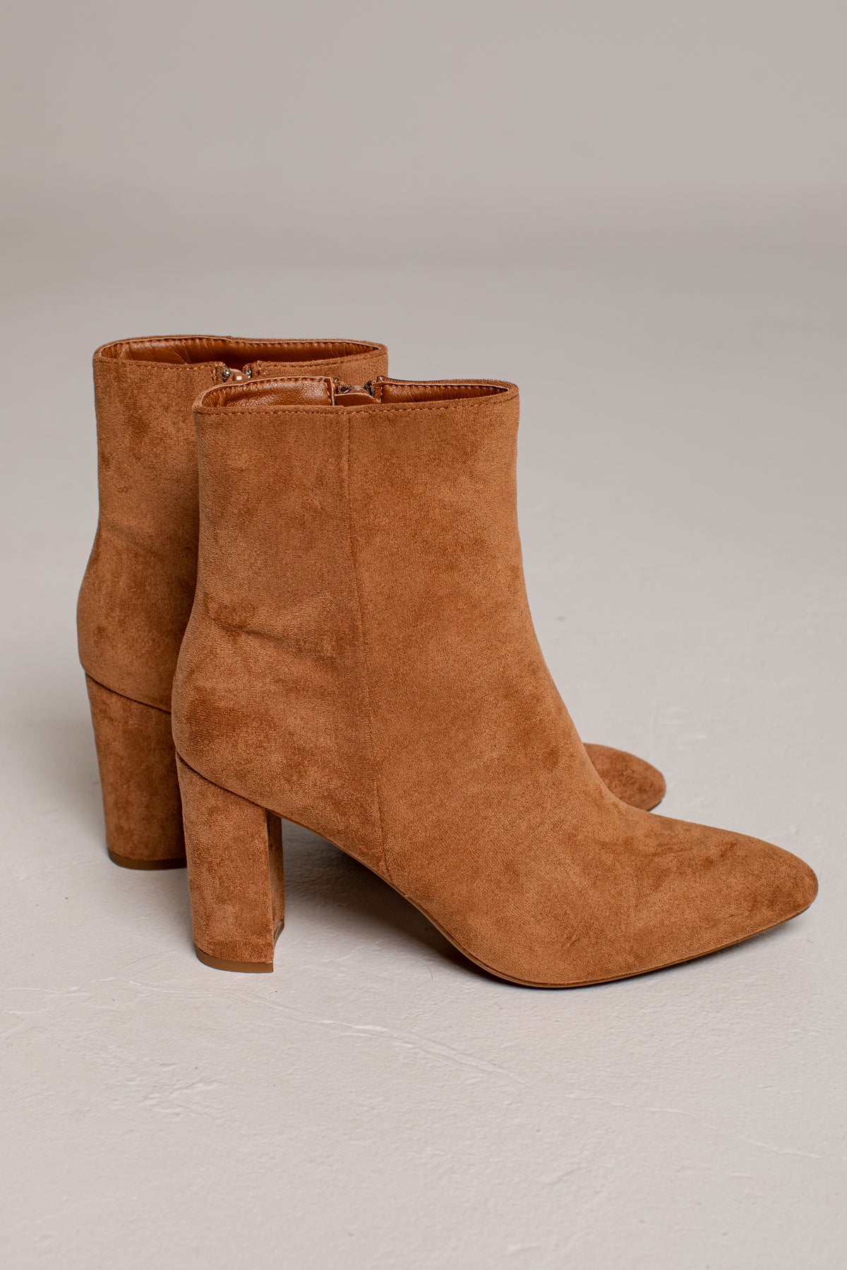 A pair of tan suede ankle boots with block heels, shown from a three-quarter angle on a neutral light gray background.