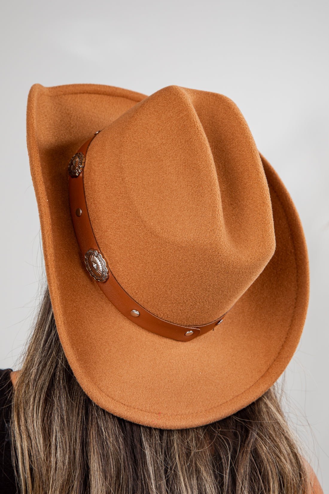 Brown cowboy hat with leather band and decorative buckle on a plain background