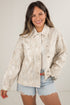Woman wearing a light-colored jacket and denim shorts on a plain background