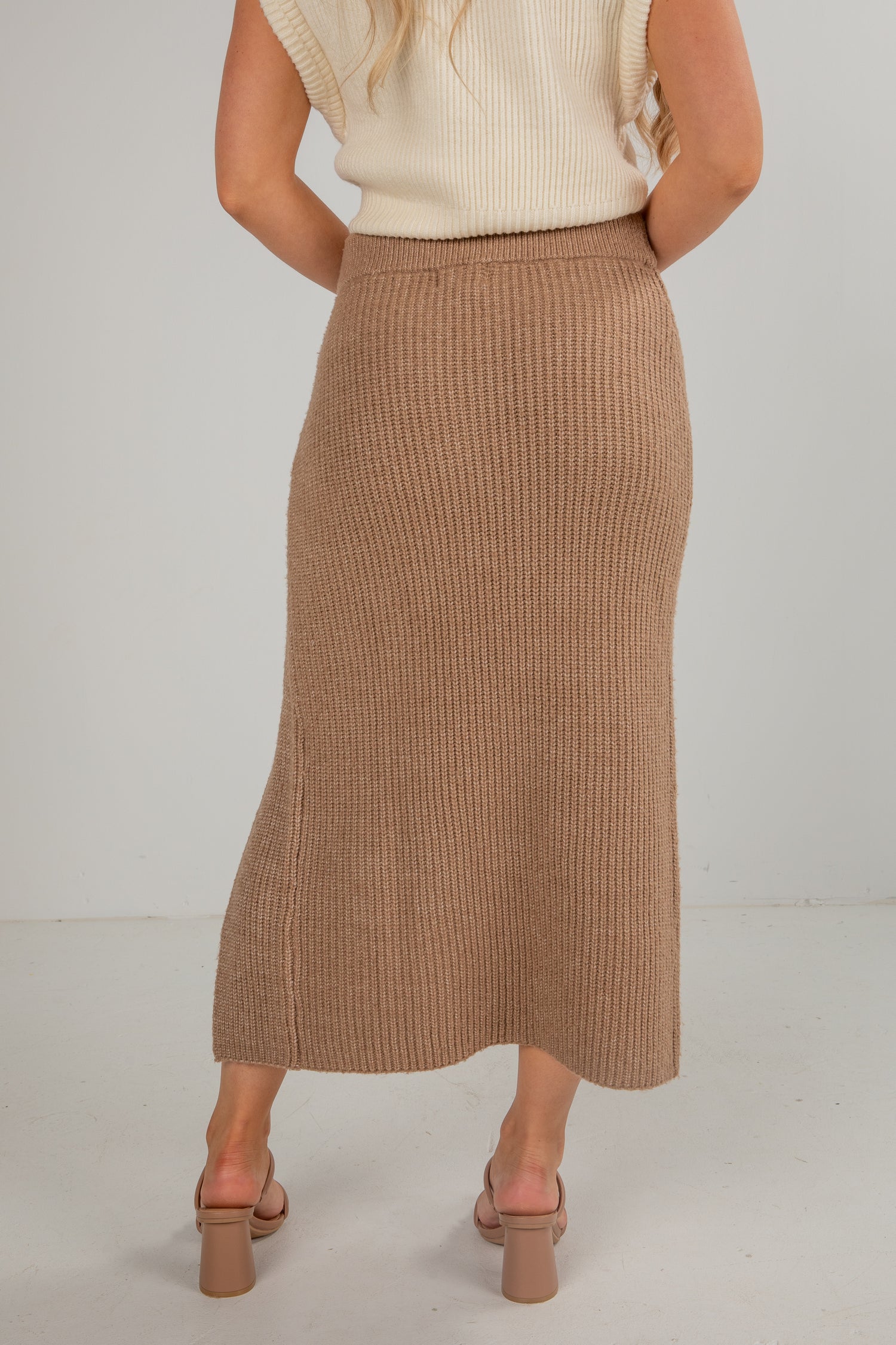 Person wearing a brown ribbed skirt and beige top on a plain background