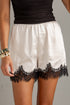 A close-up of a person wearing white satin shorts with a black lace hem, paired with a black top and gold bracelets.