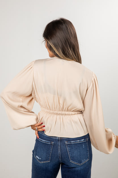 Woman wearing a beige blouse and blue jeans against a plain background