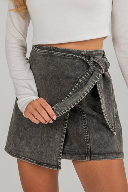 Person wearing a gray denim wrap skirt with a plain background