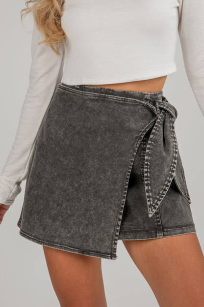 Person wearing a black denim skirt with a white top on a plain background