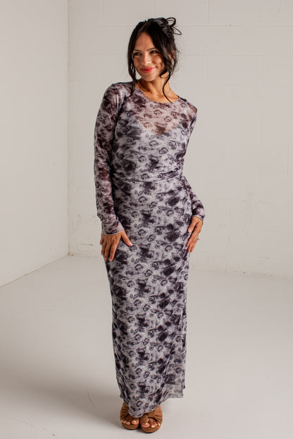 A woman modeling a long-sleeve maxi dress with a gray and black abstract floral pattern, standing in a white studio corner.