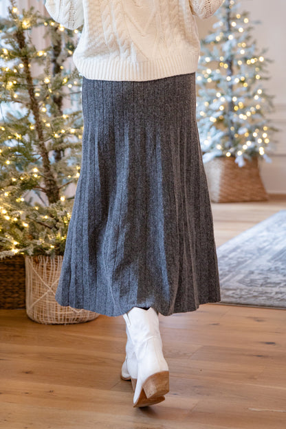 Person wearing a gray skirt and white sweater with Christmas trees in the background