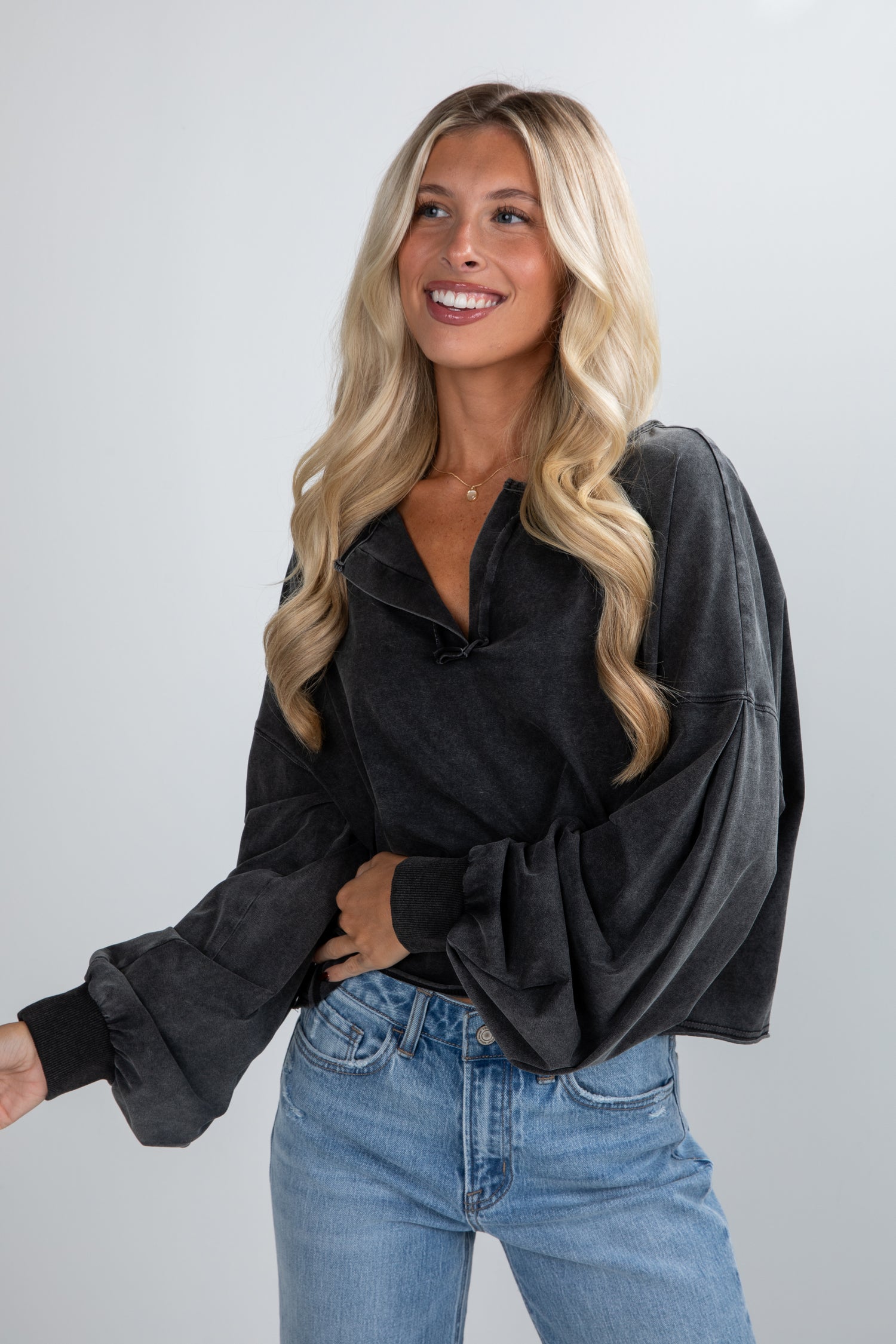 Woman wearing a black long-sleeve top and blue jeans against a plain background