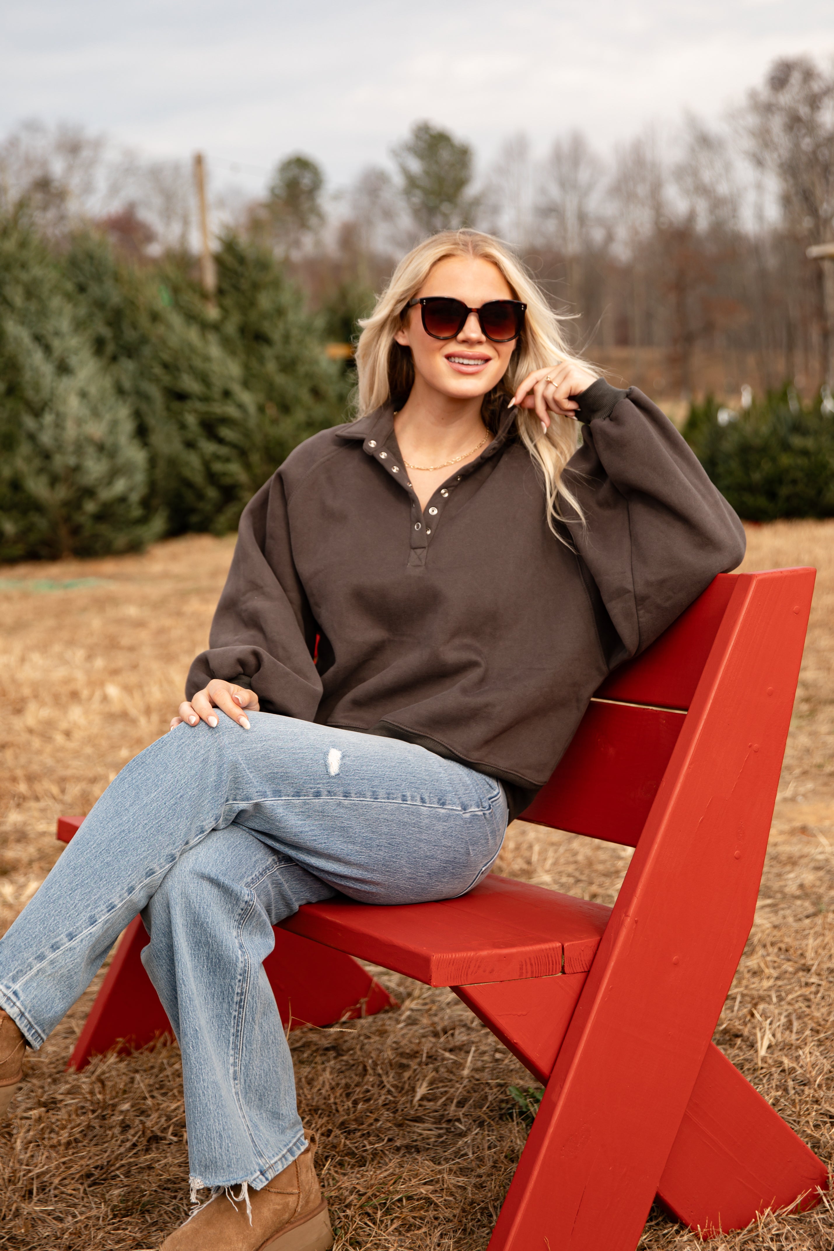 Woman sitting on a red bench in an outdoor setting with trees in the background