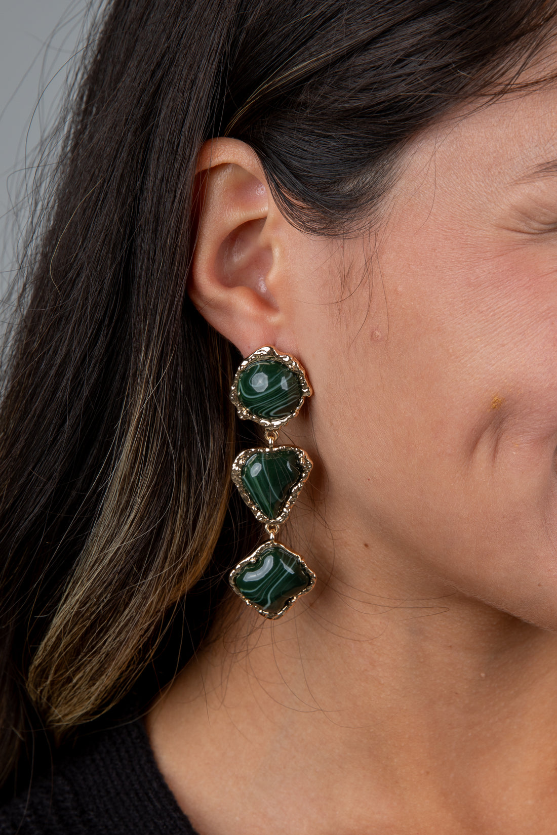 Close-up of a person wearing green gemstone earrings with a neutral background