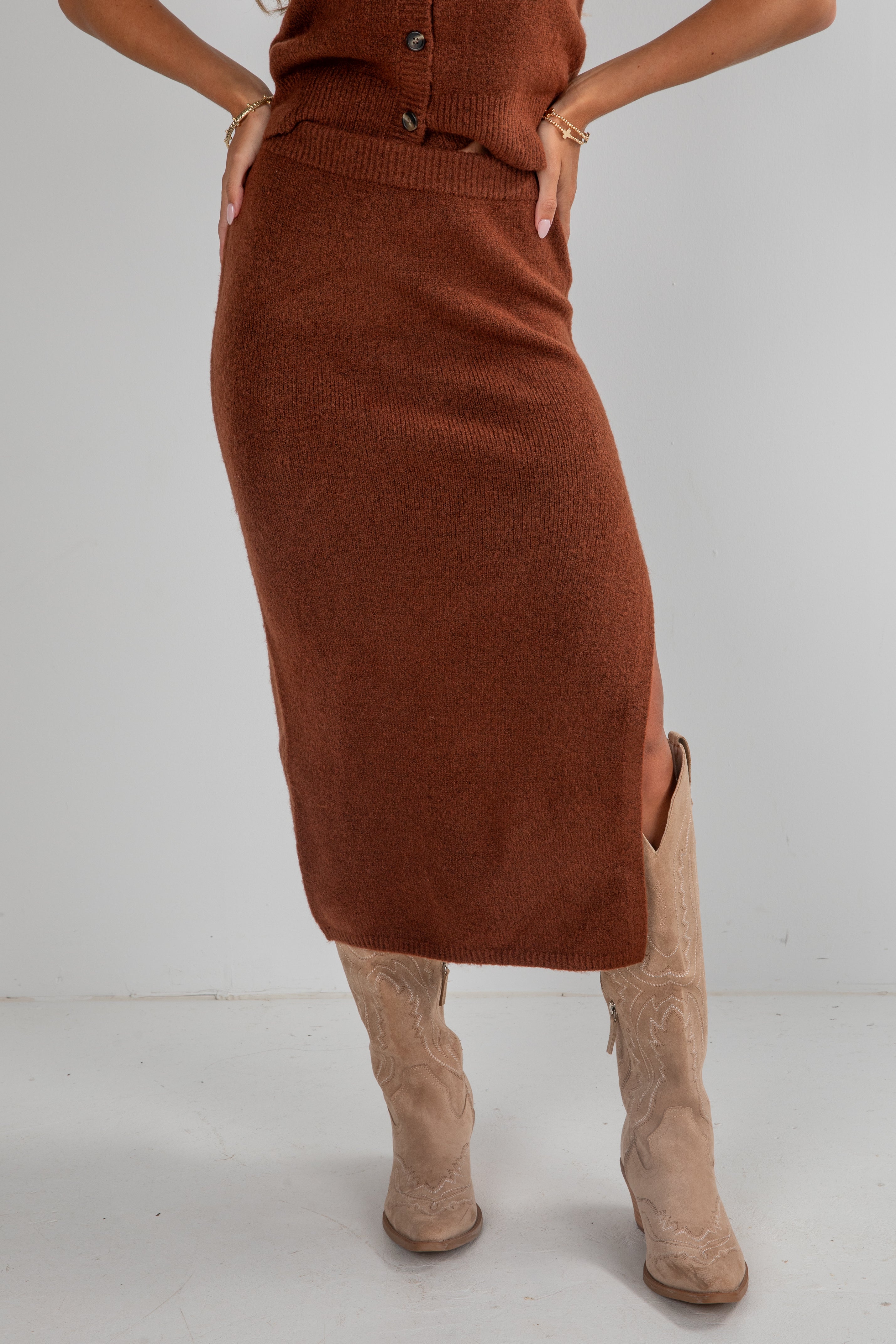 Person wearing a brown knit skirt and beige boots on a white background