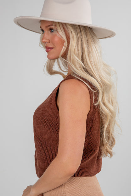 Woman wearing a brown sleeveless top and beige hat on a white background