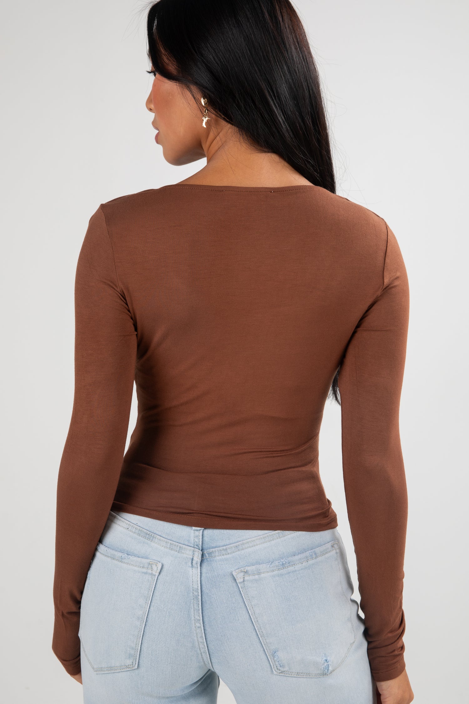 Person wearing a brown long-sleeve top and light blue jeans on a white background