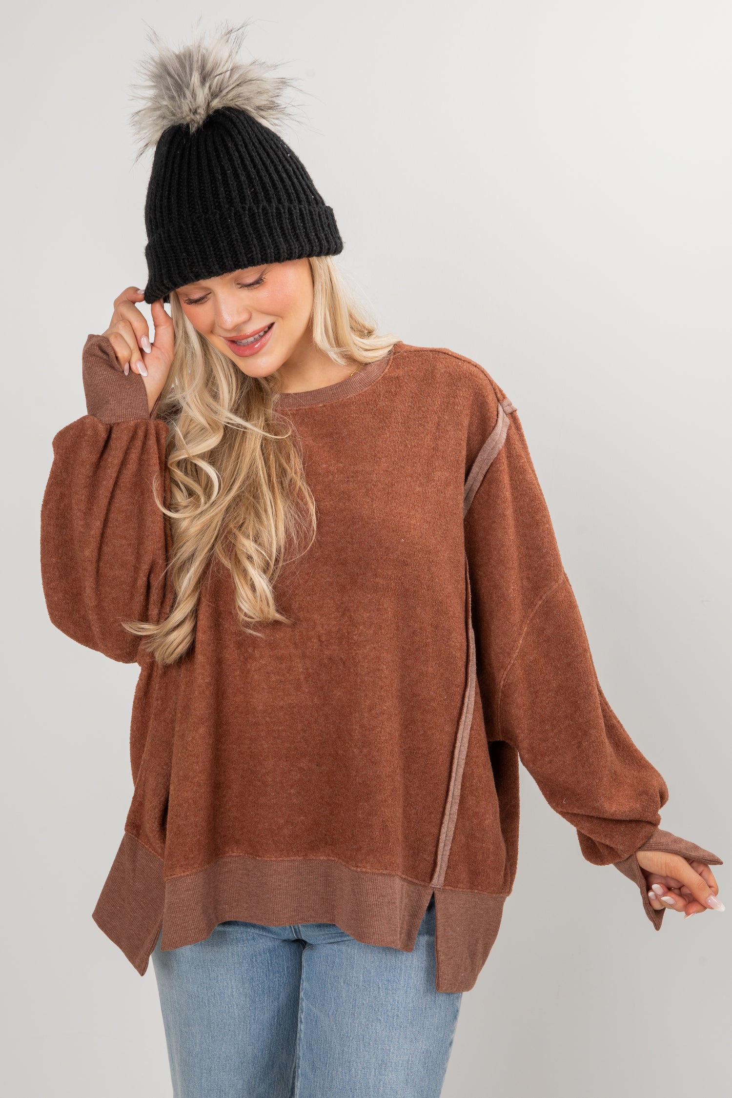 Woman wearing a brown sweater and black beanie with gray pom-pom on a white background