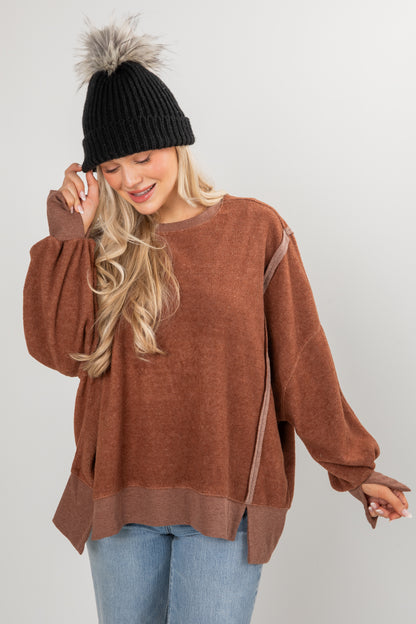 Woman wearing a brown sweater and black beanie with gray pom-pom on a white background