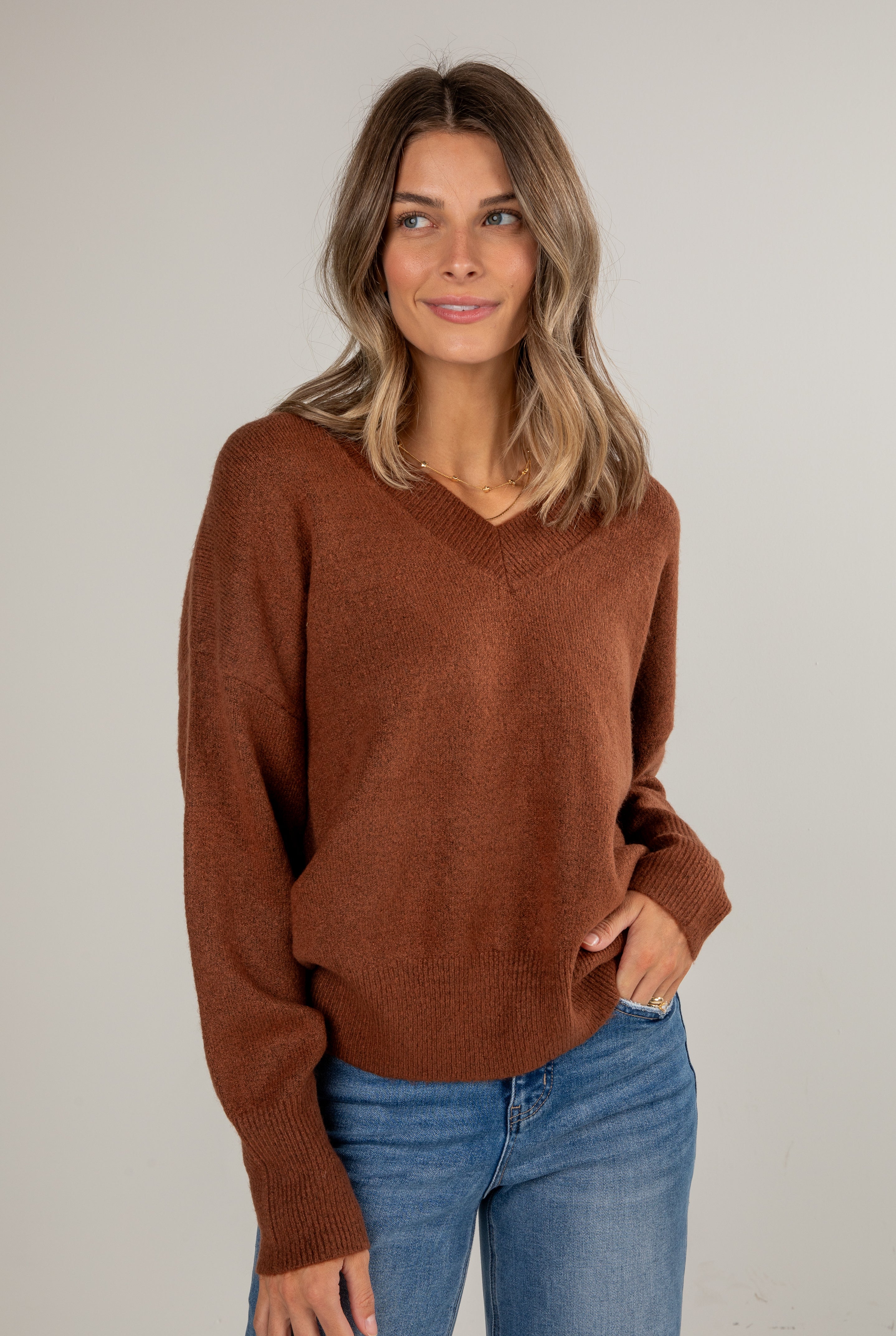 Woman wearing a brown sweater and blue jeans against a plain background