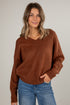 Woman wearing a brown sweater and blue jeans against a plain background