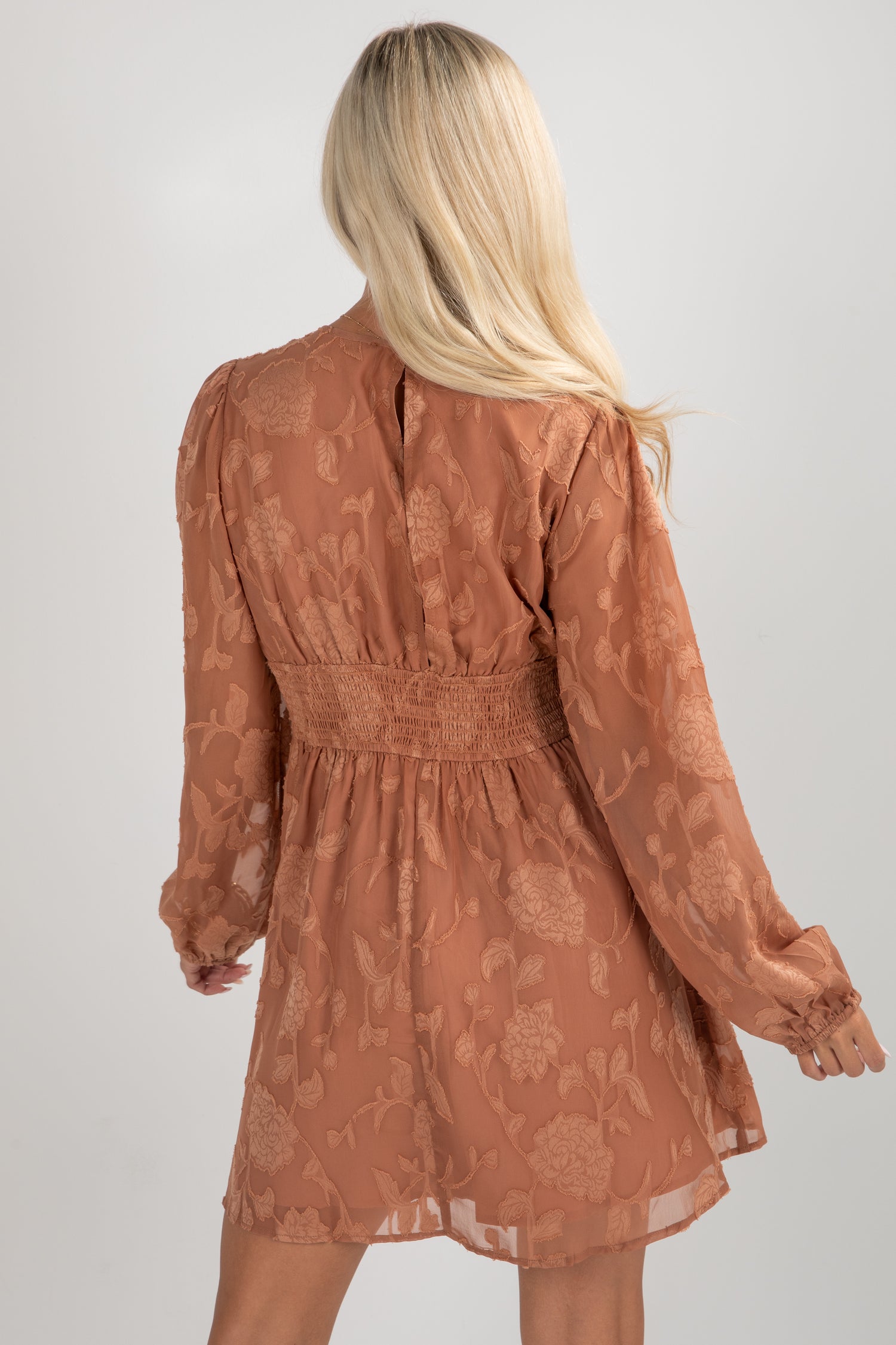 Woman wearing a brown floral dress against a plain background