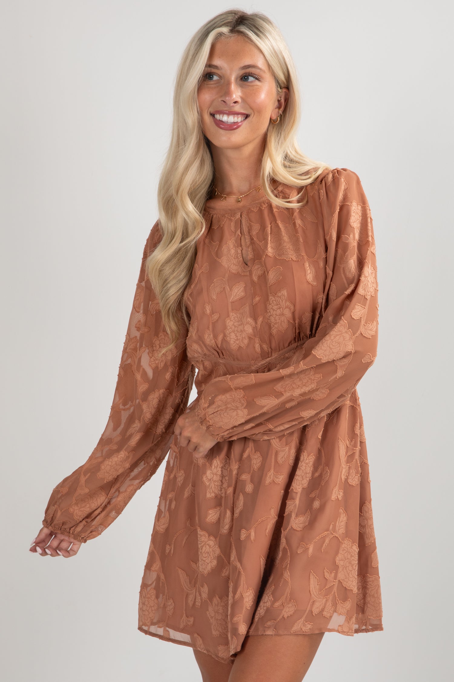 Woman wearing a brown dress with long sleeves on a plain background
