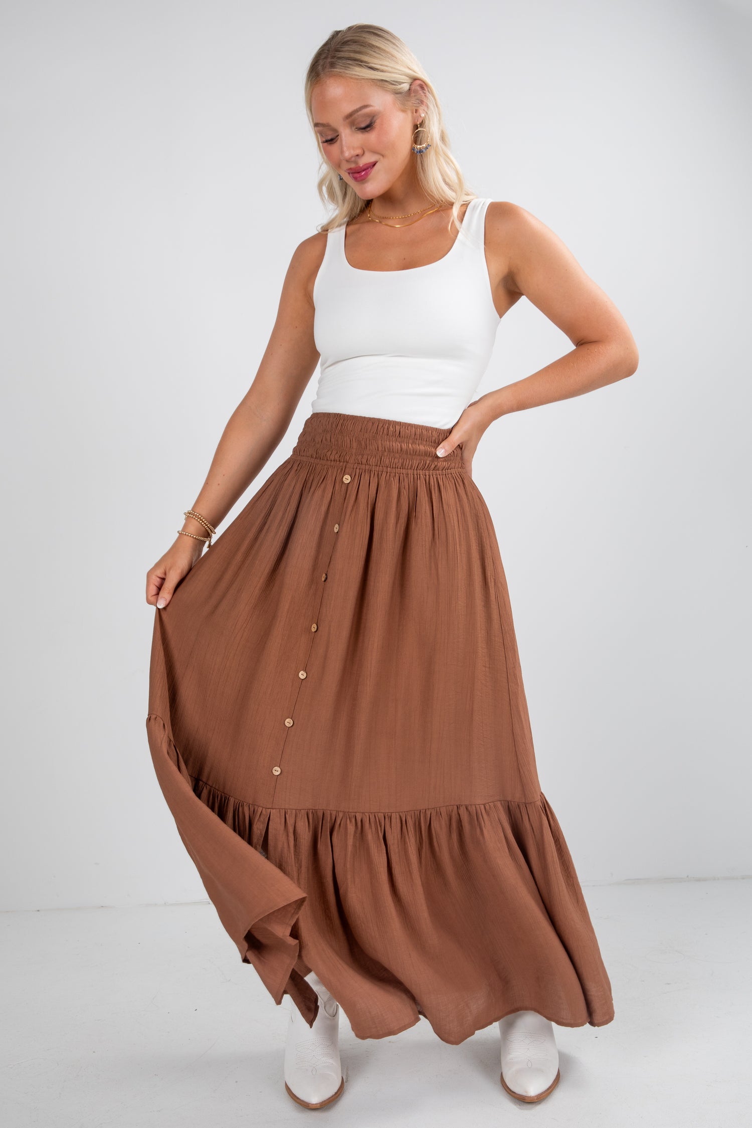 Woman wearing a white tank top and brown maxi skirt on a plain background