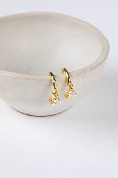 Gold hoop earrings with small diamonds on a white ceramic dish.