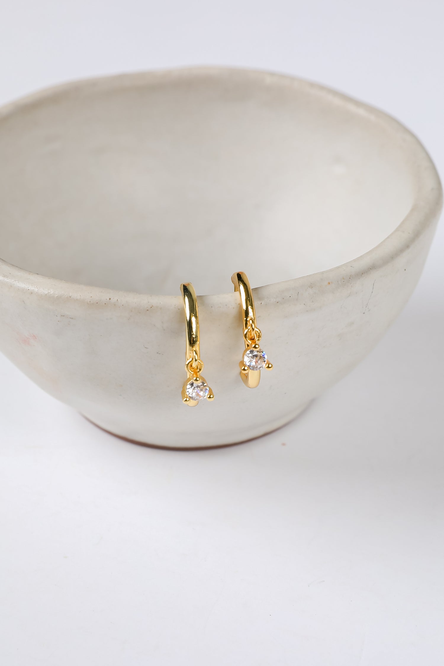 Gold earrings with clear stones in a beige bowl on a white background
