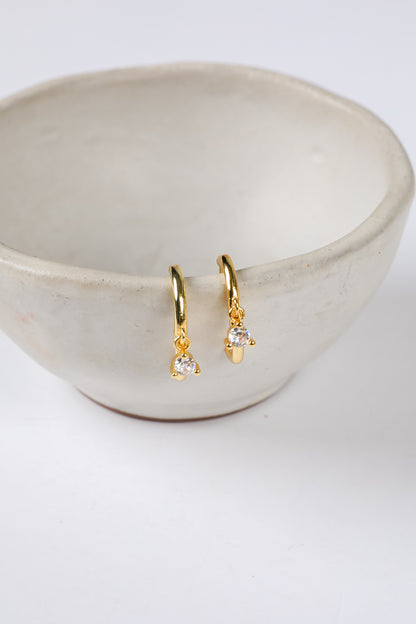 Gold earrings with clear stones in a beige bowl on a white background