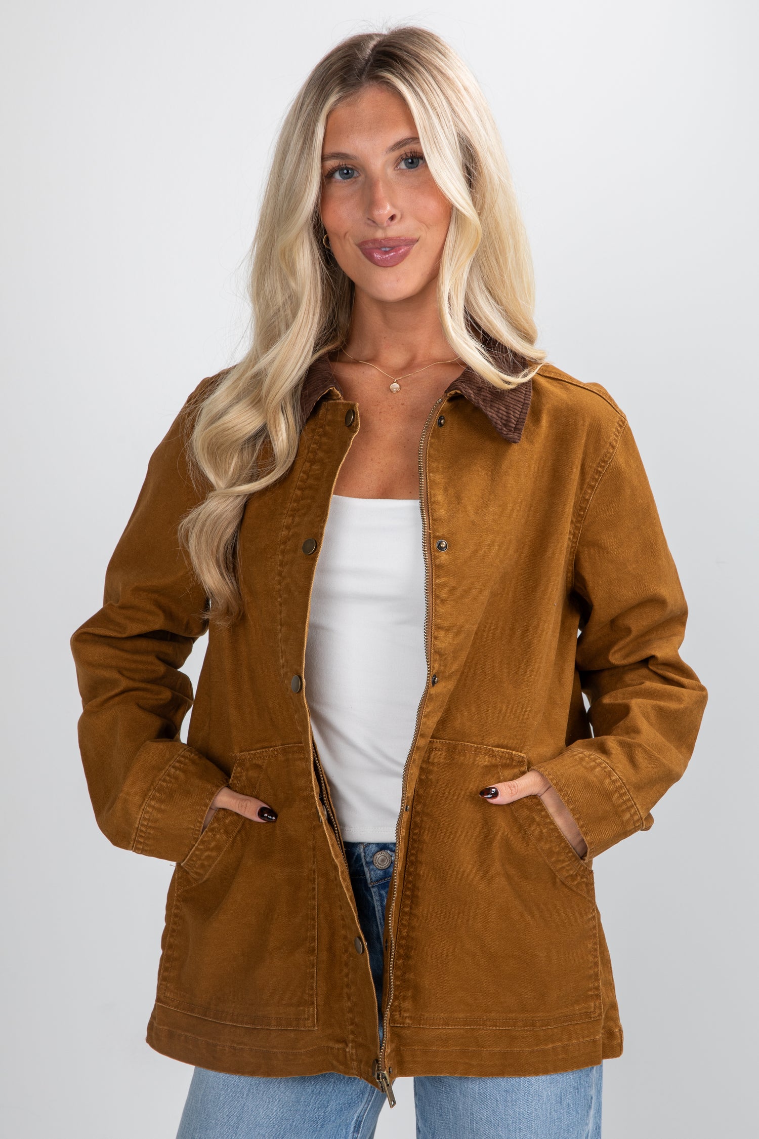 Woman wearing a brown jacket over a white top and blue jeans on a white background