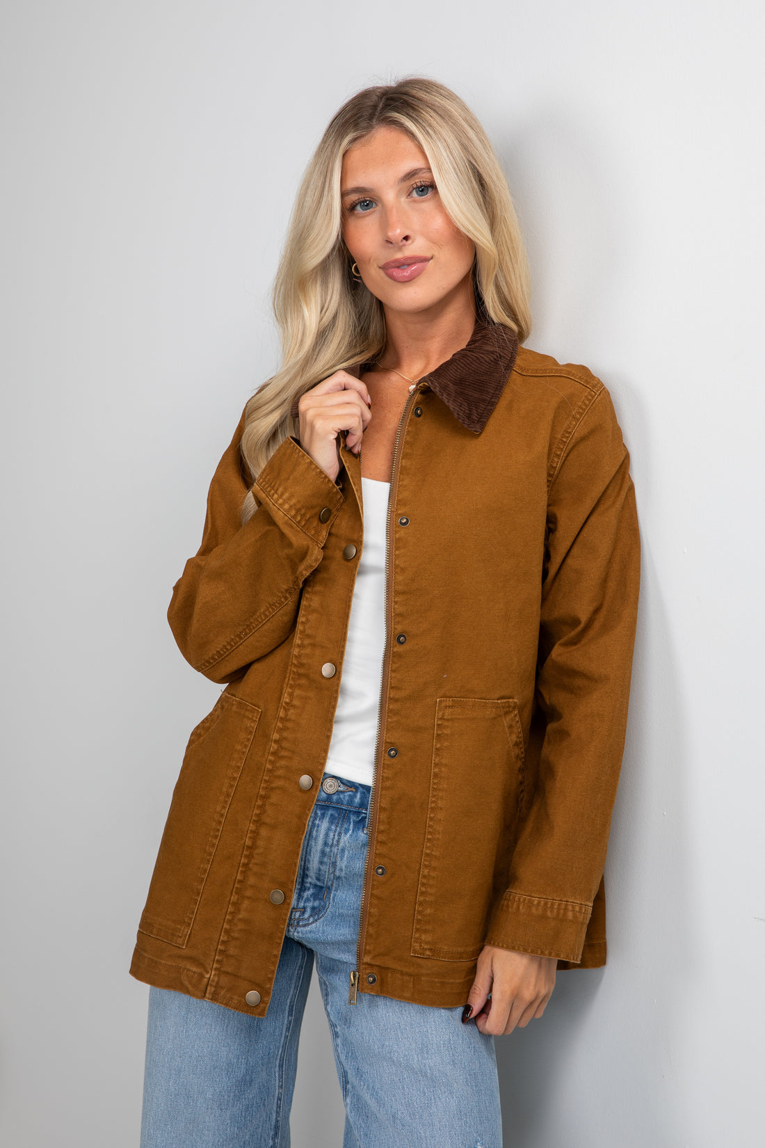 Woman wearing a brown jacket and blue jeans against a plain background