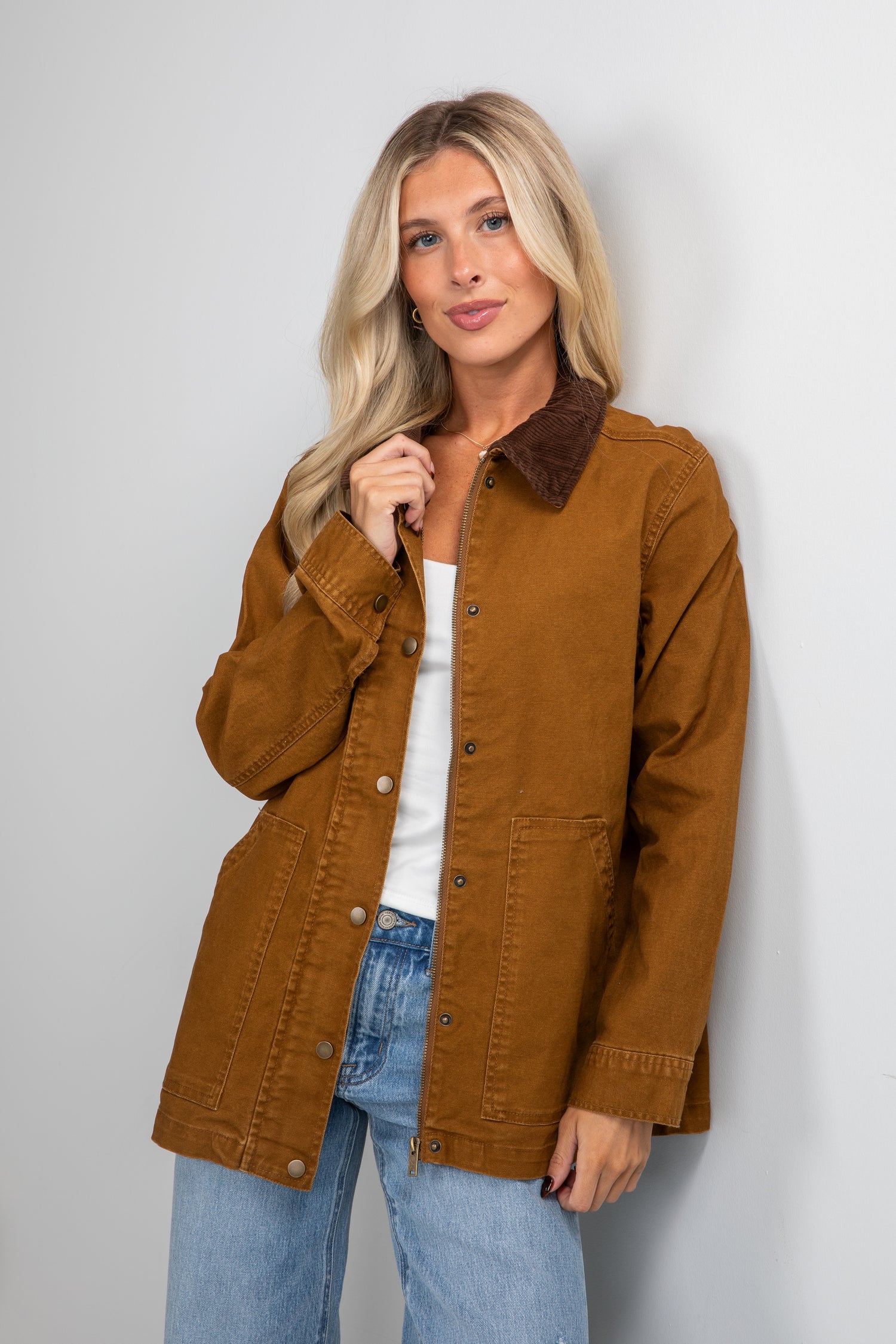 Woman wearing a brown jacket and blue jeans against a plain background