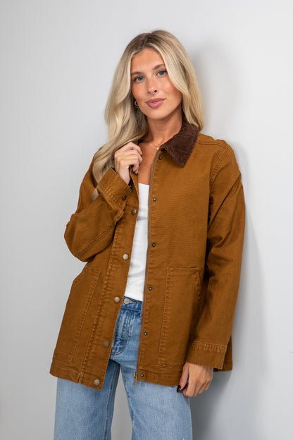 Woman wearing a brown jacket and blue jeans against a plain background