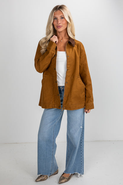 Woman wearing a brown jacket, white top, and blue jeans on a white background