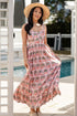 Woman in a pink floral dress and straw hat standing by a poolside.