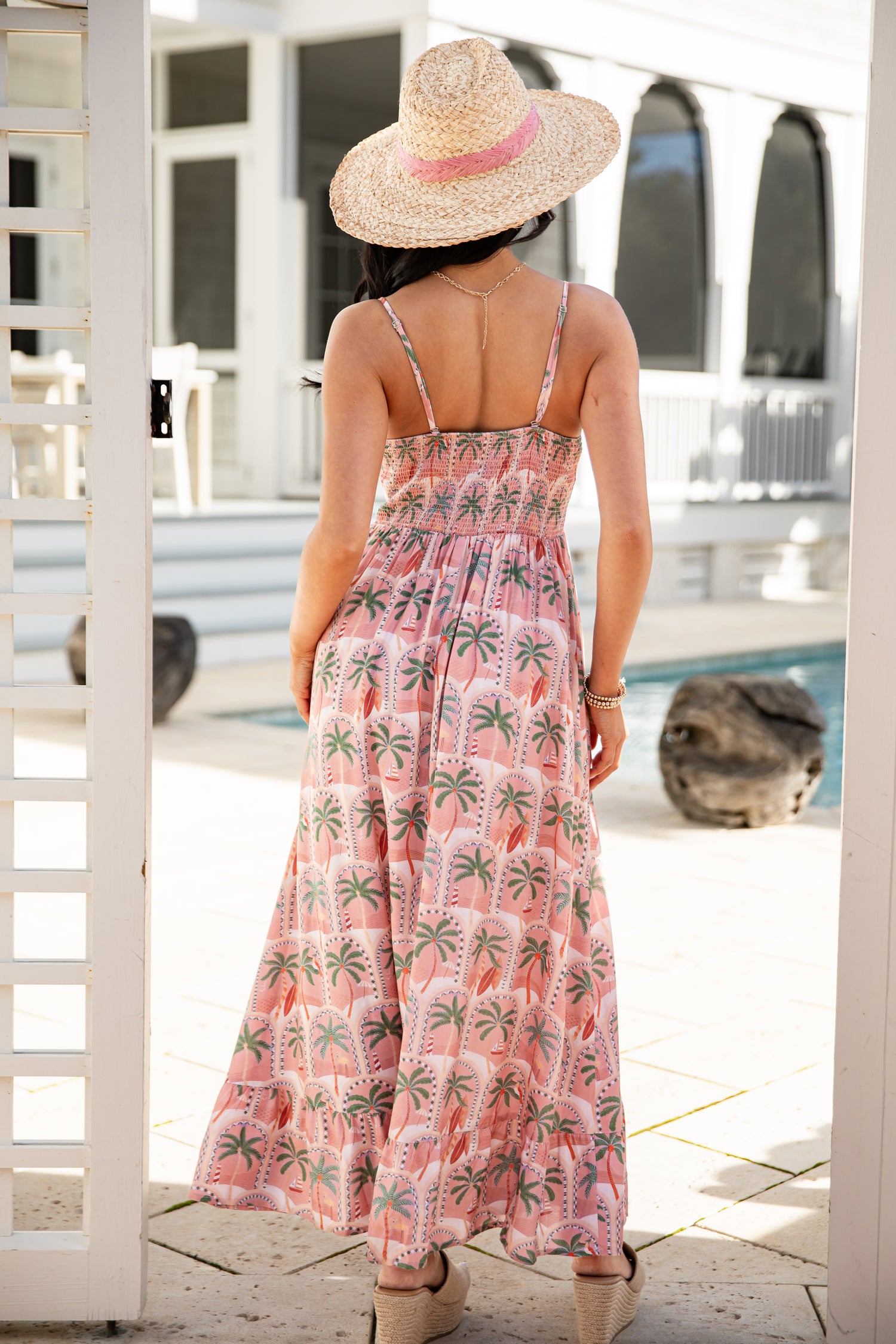 Woman in a pink floral dress and sun hat by a poolside.