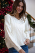 Woman wearing a white sweater in a festive indoor setting with Christmas decorations.