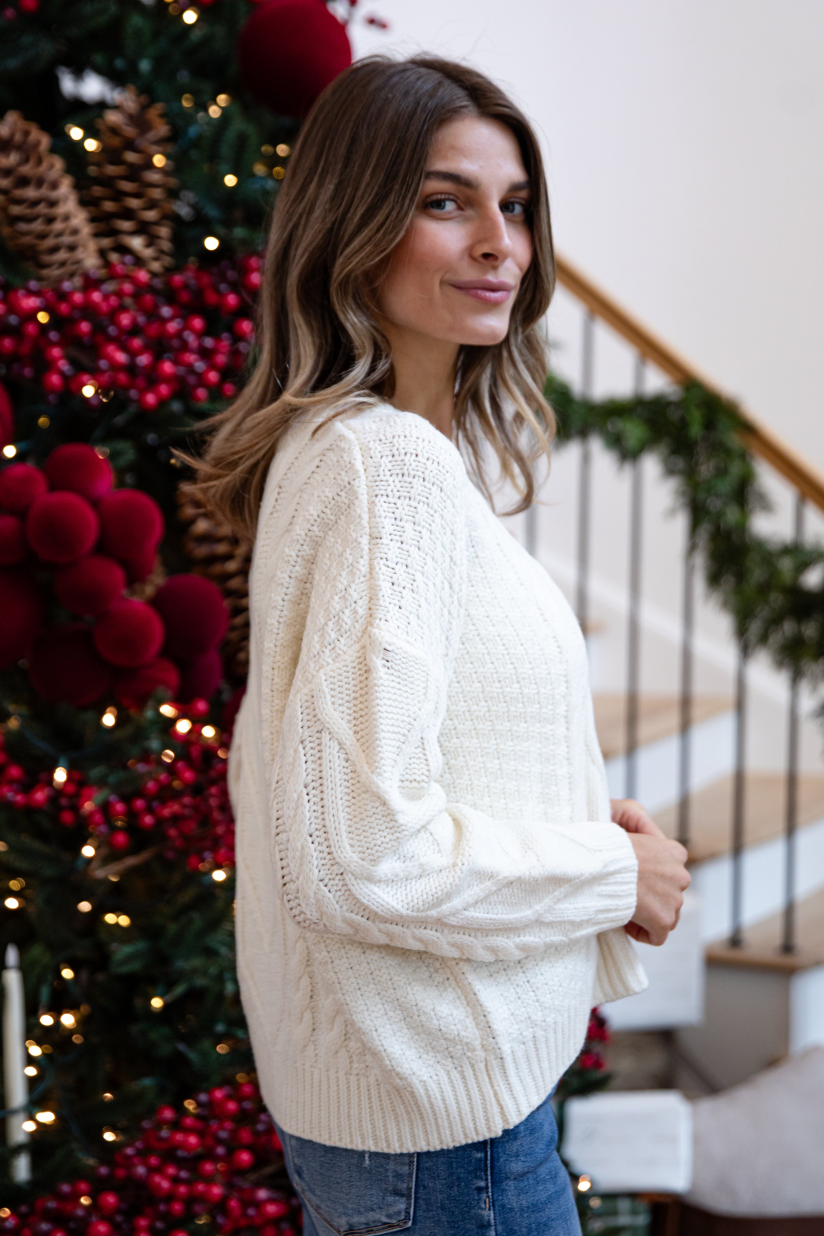Woman wearing a white sweater in a festive indoor setting with Christmas decorations.