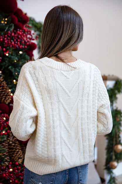 Person wearing a cream sweater in front of a decorated Christmas tree.