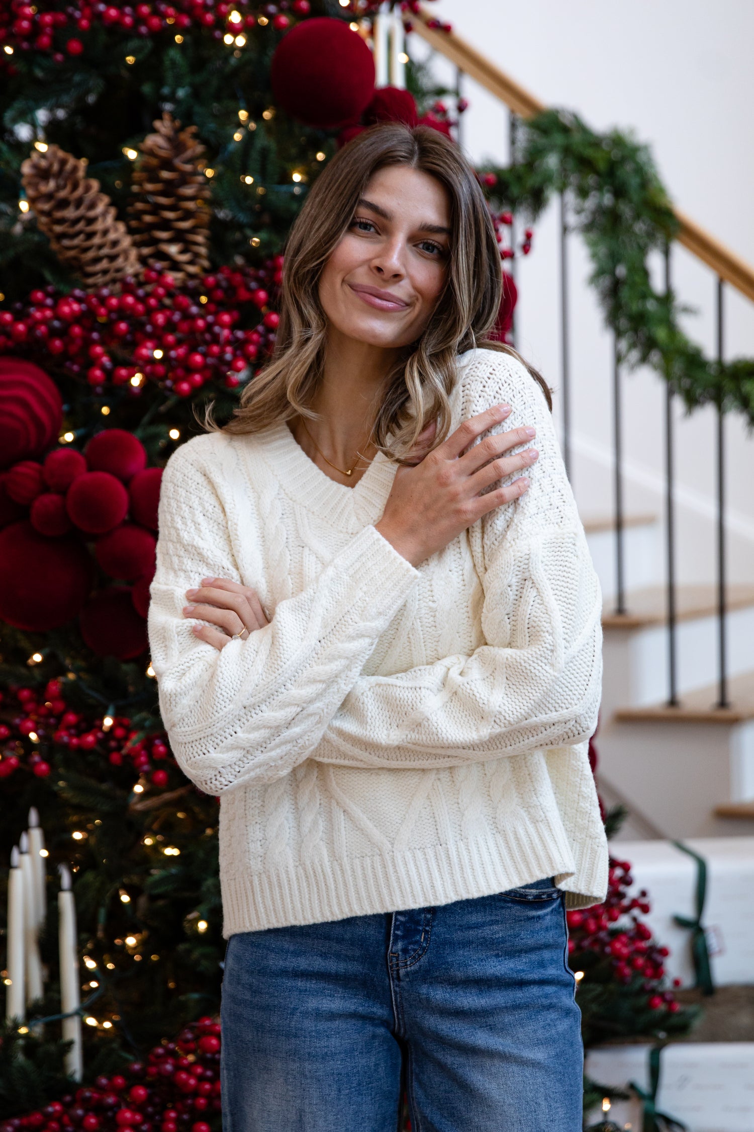 Woman wearing a white sweater in front of a decorated Christmas tree.