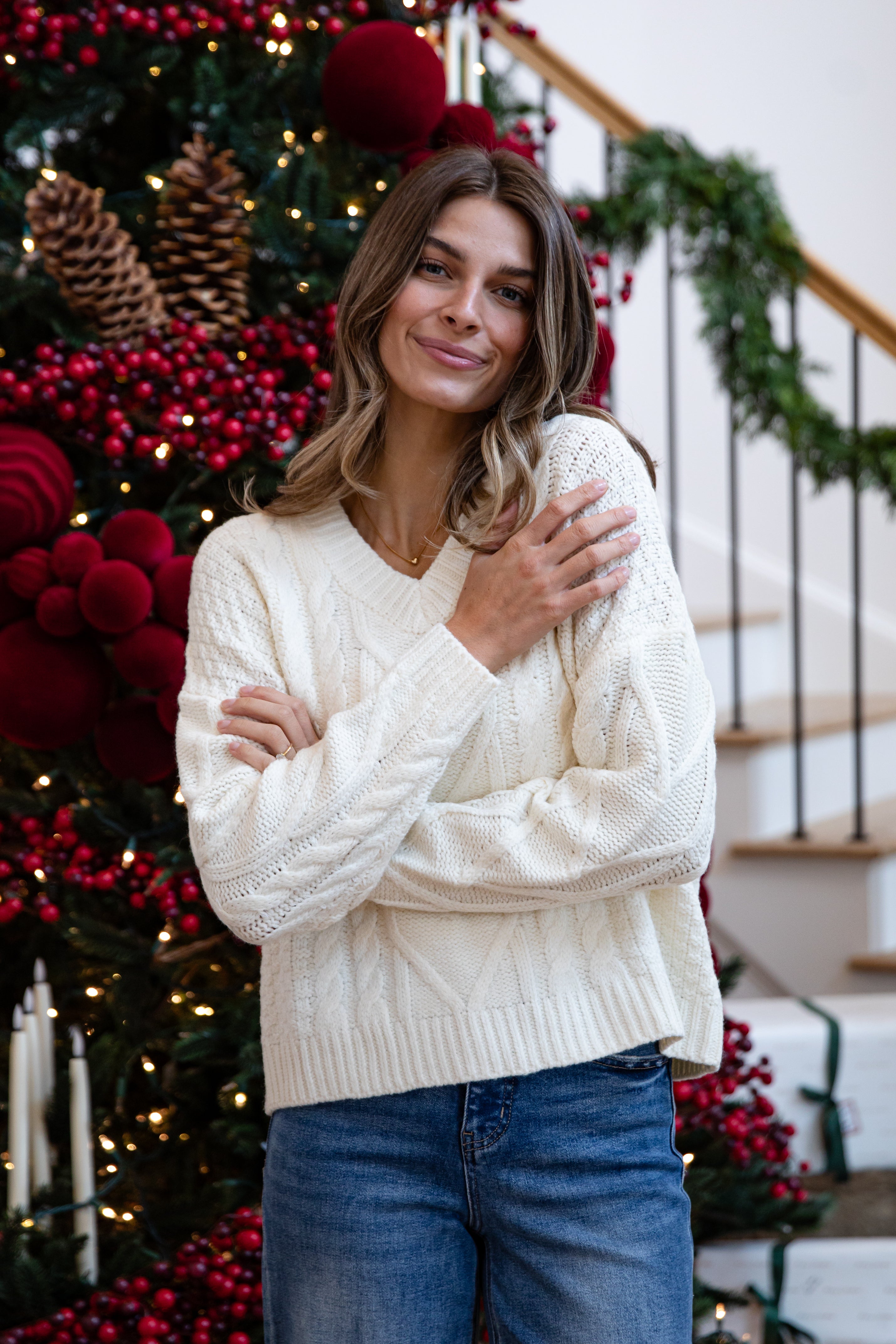 Woman wearing a white sweater in front of a decorated Christmas tree.