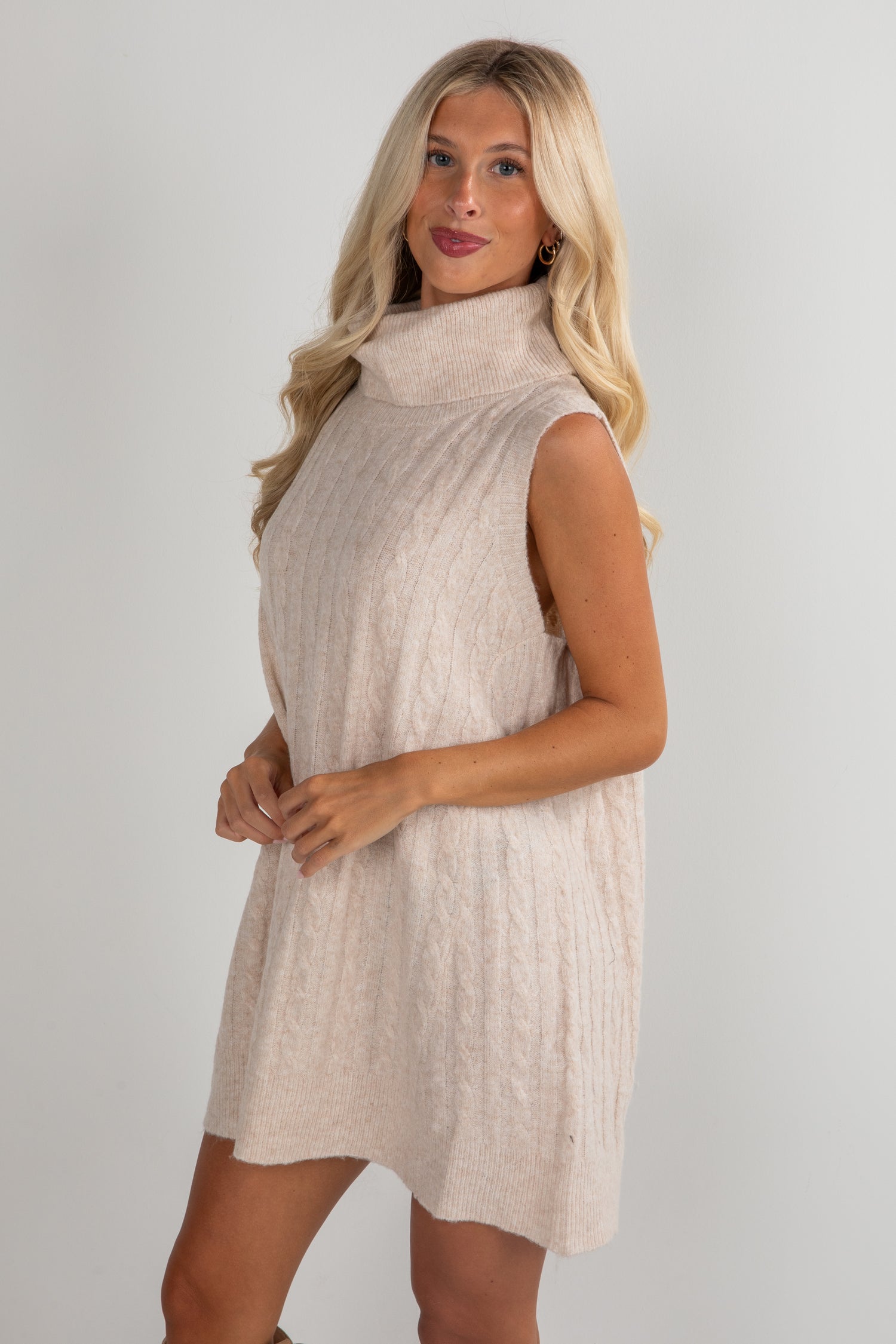 Woman wearing a beige sleeveless dress against a plain background