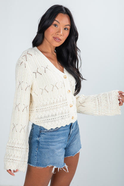 Woman wearing a white knitted cardigan and denim shorts on a plain background