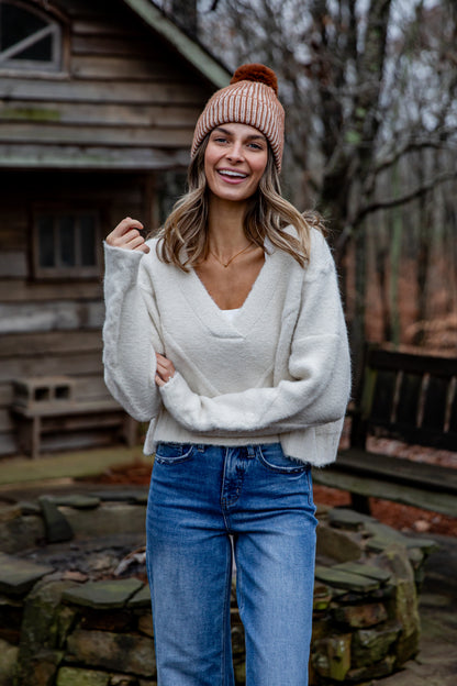 Woman wearing a white sweater and blue jeans standing in front of a wooden cabin.
